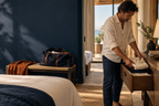AI-generated illustrative travel scene: a man unpacking clothes in a hotel room. Not a Roamviro customer, exact-product photograph or measured packing demonstration.